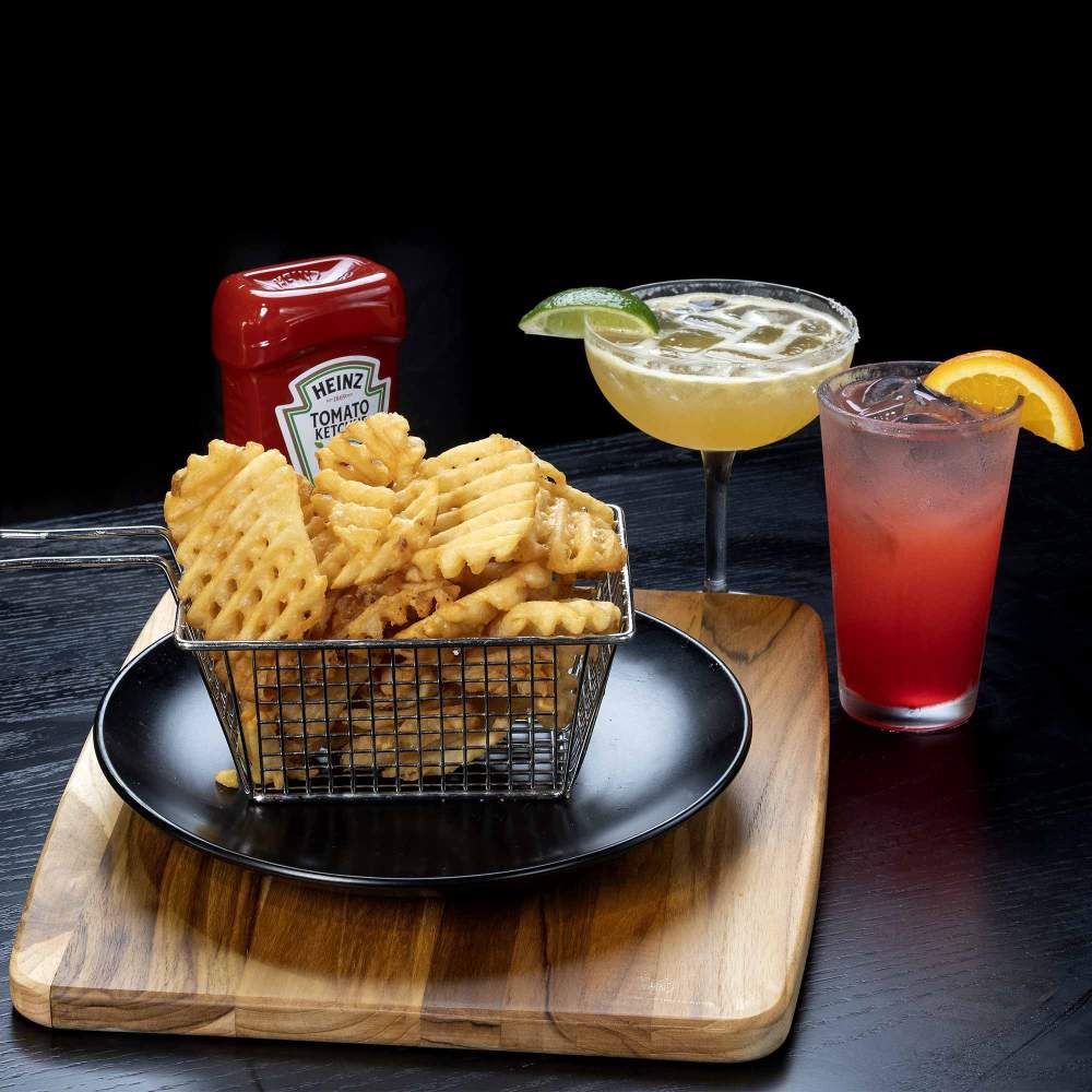 a basket-of-waffle-fries with a bottle of ketchup and two cocktails