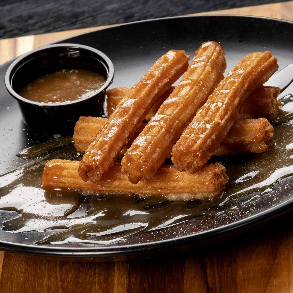 a plate containing six churros and a bowl of sauce