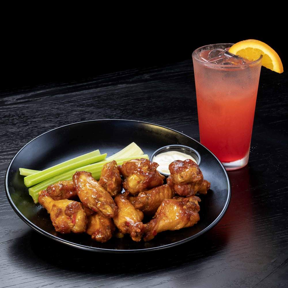 a bowl of chicken wings and celery next to a cocktail on a table
